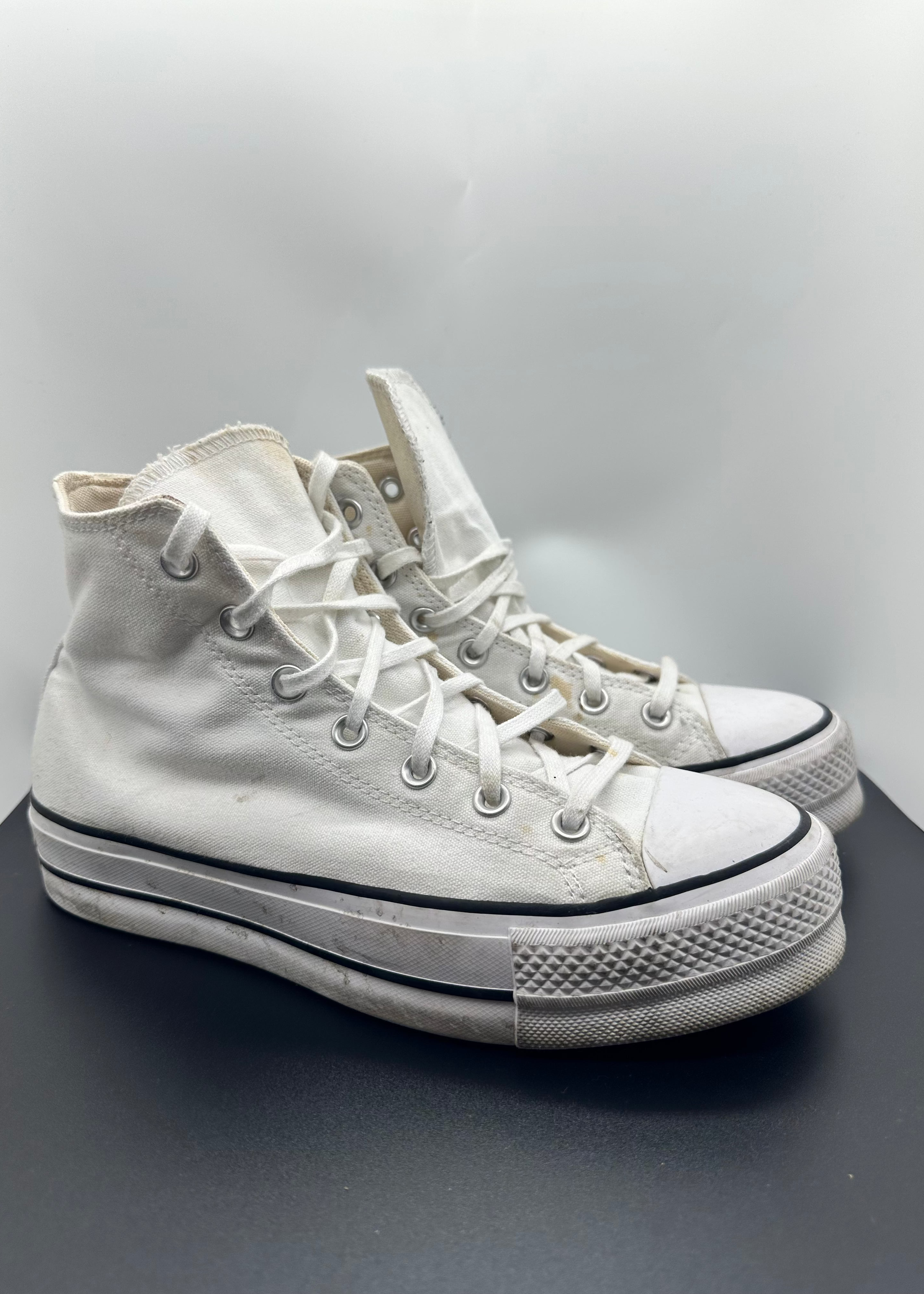 White high-top sneakers on a gray surface with a light gray background