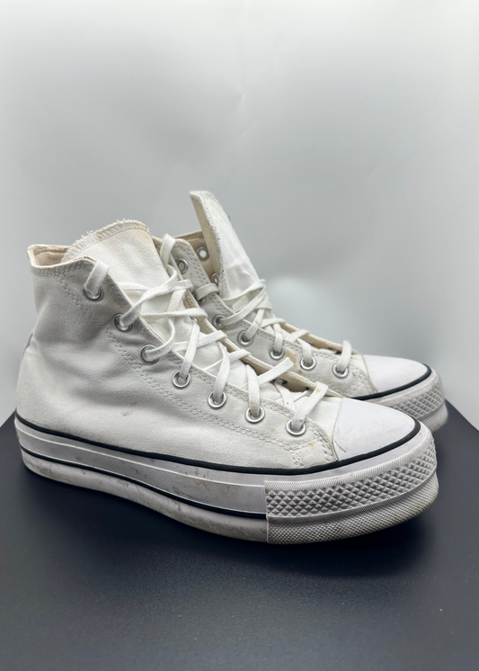 White high-top sneakers on a gray surface with a light gray background