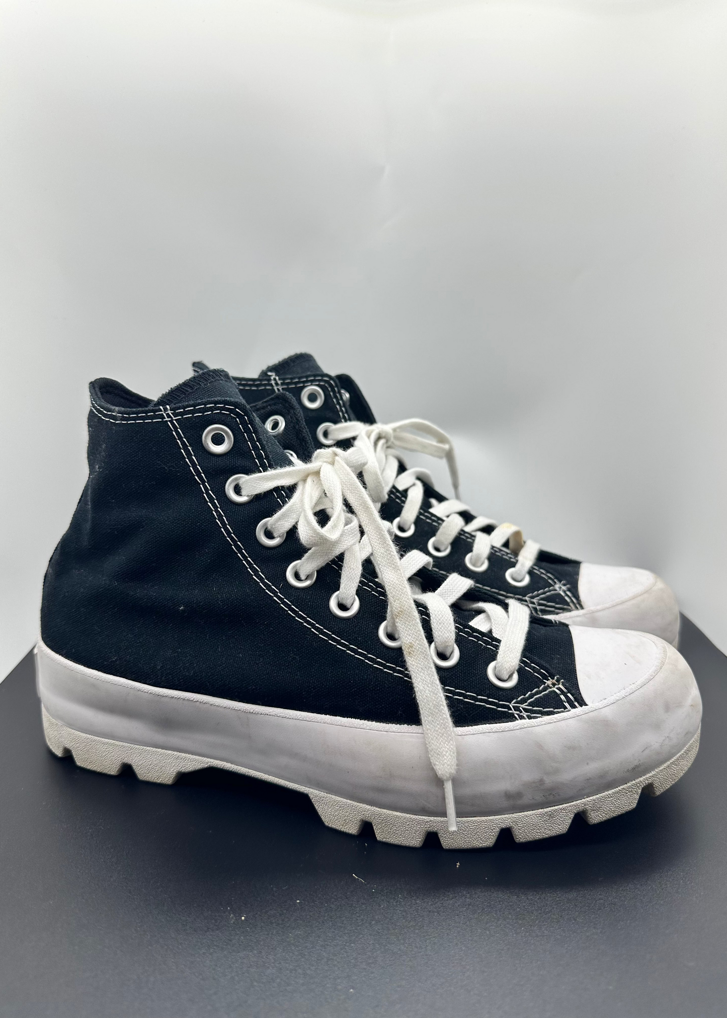 Black high-top sneakers with white soles on a gray surface