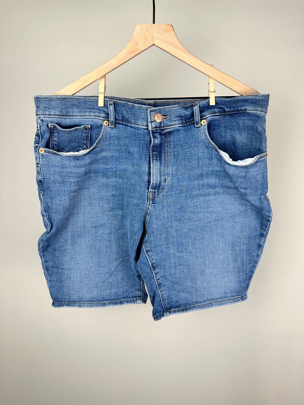 A pair of blue Levi Strauss Bermuda shorts hung on a wooden hanger against a plain background.